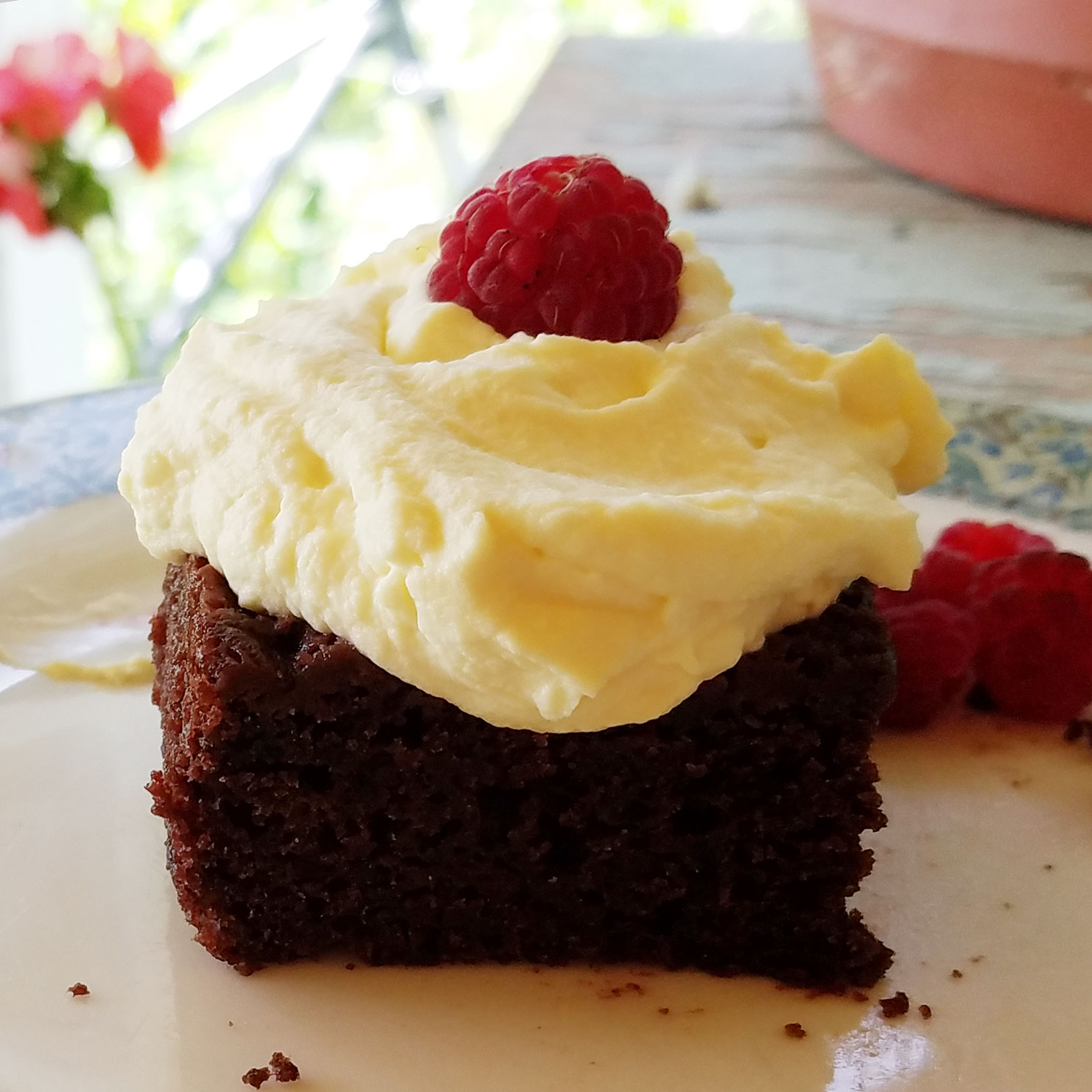 slice of dark chocolate buttermilk cake topped with whipped cream frosting and a raspberry 