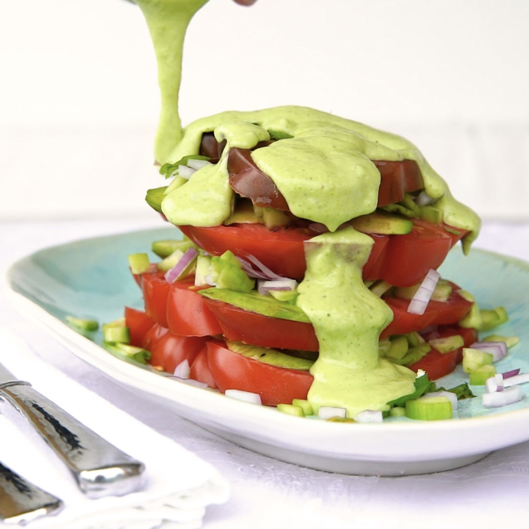 creamy avocado-kefir dressing poured over a stack of sliced tomatoes and chopped veggies