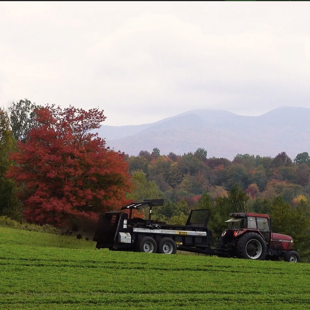tractor spreading compost on hay field in autumn